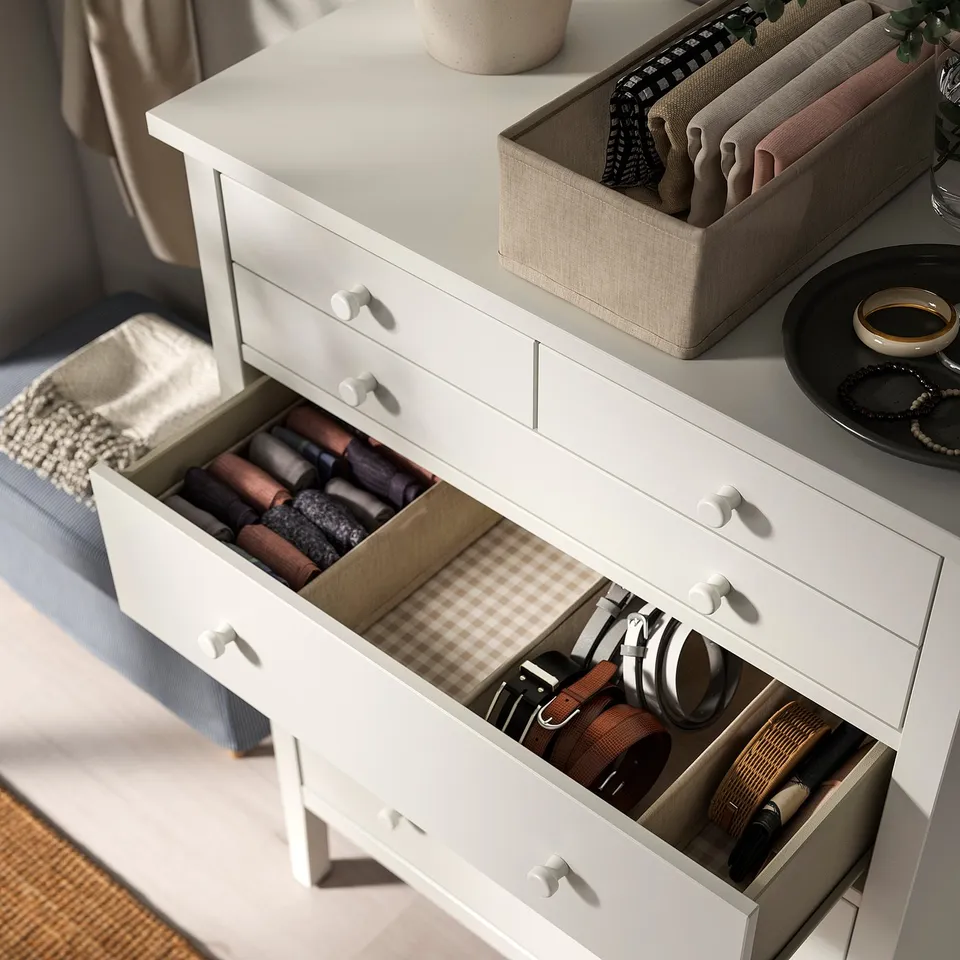 Open chest of drawers with belts, rolled clothes, and accessories.