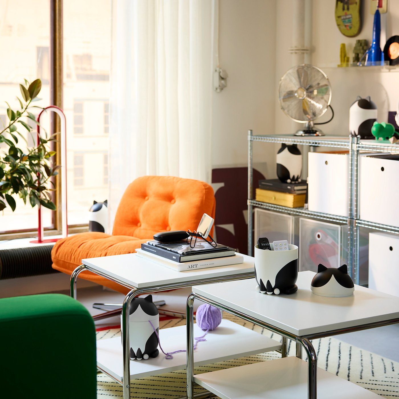 Modern living room with orange chair, cat-themed storage, green bean bag, fan, and colourful decor.