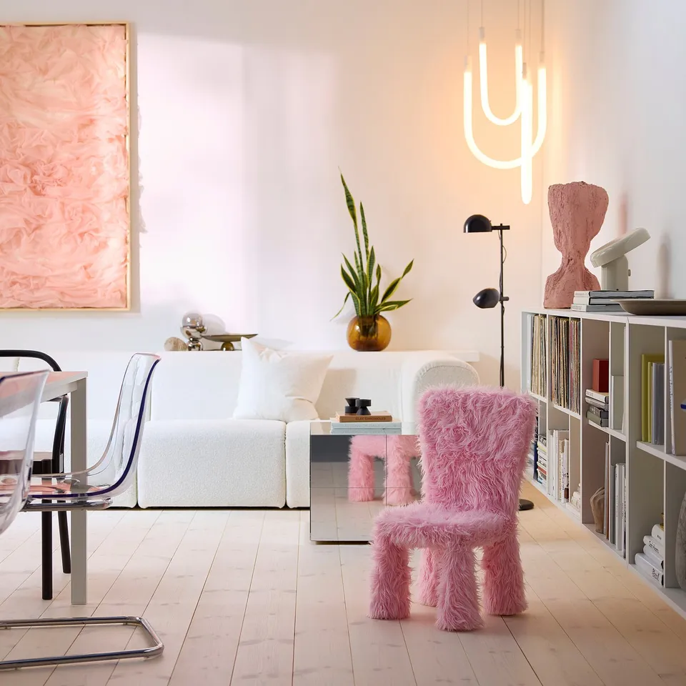 Modern living room a bright pink, plush GREJSIMOJS chair cover in front of a high-backed white sofa, creating a vibrant and playful atmosphere.
