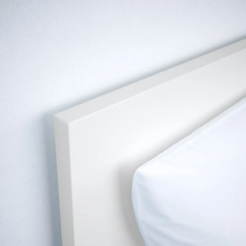 Minimalist white bed frame, cleanly designed, high headboard against wall.