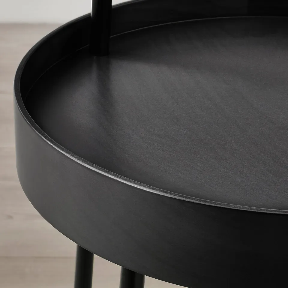 Black round side table with smooth, high edges and a sturdy handle, standing on a wooden floor.