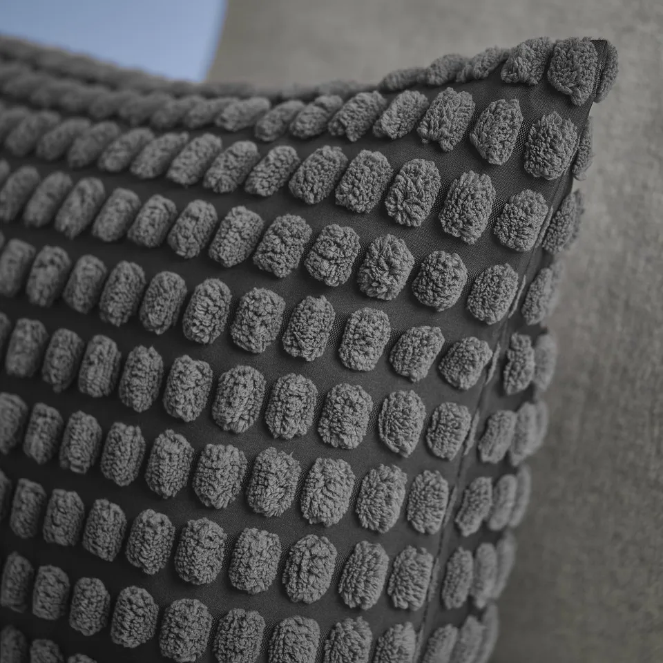 Textured cushion cover with raised, knitted designs in a repeating pattern, featuring a zip for easy removal.