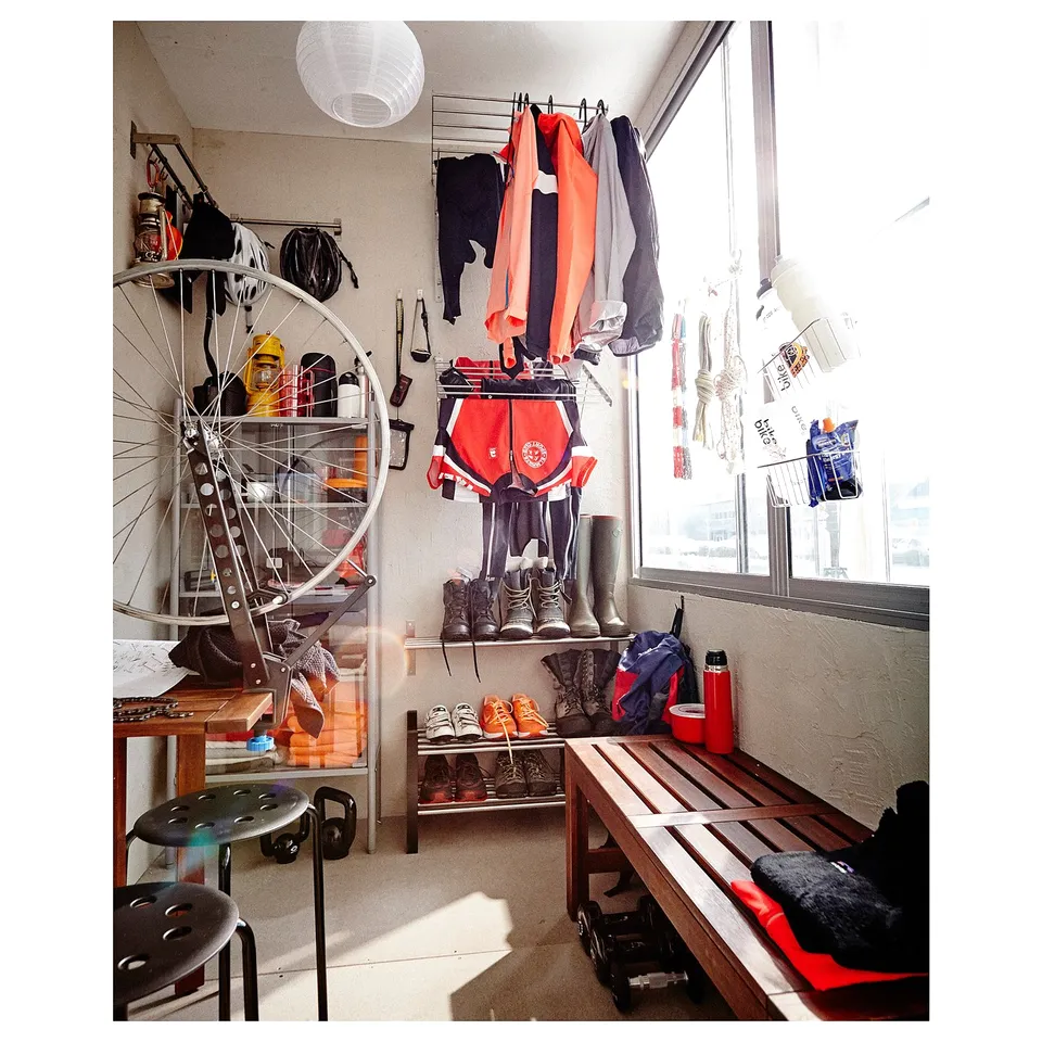 Small, organised entryway with shoe rack, bench, bicycle wheel decor, hooks with jackets and hats, and toe-tap stool.