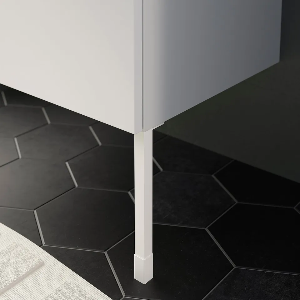 White ENHET cabinet leg on black hexagonal floor tiles.