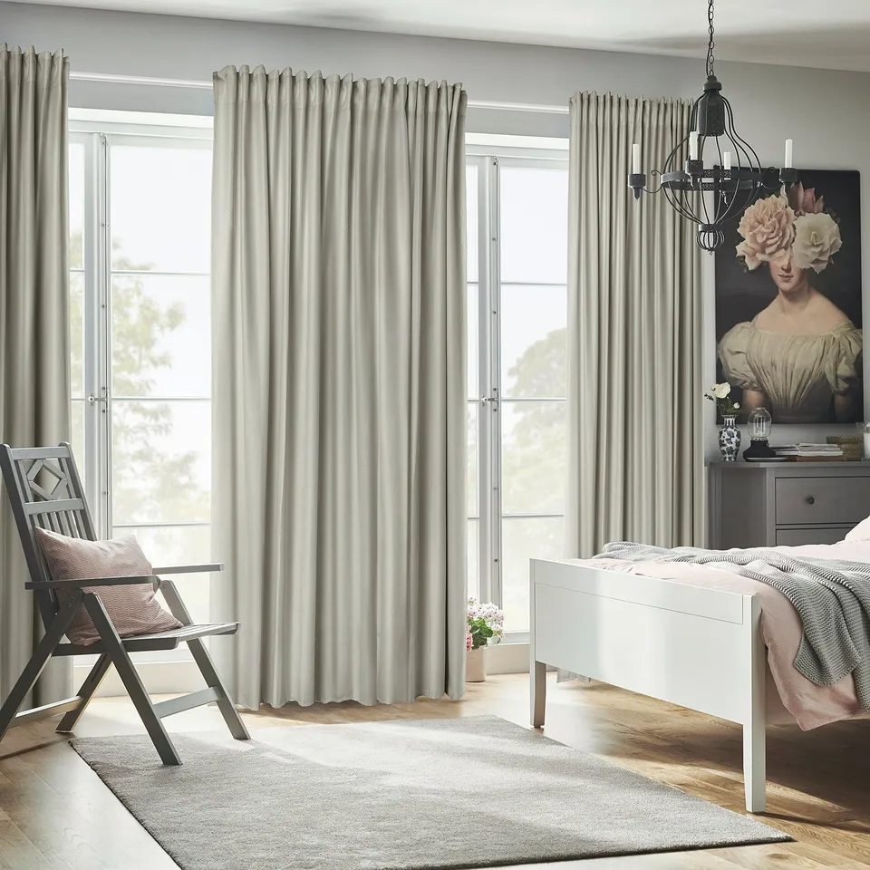 Bedroom with annakjsa grey room-darkening curtains, floral artwork, pink-bed, grey rug, chair by window.