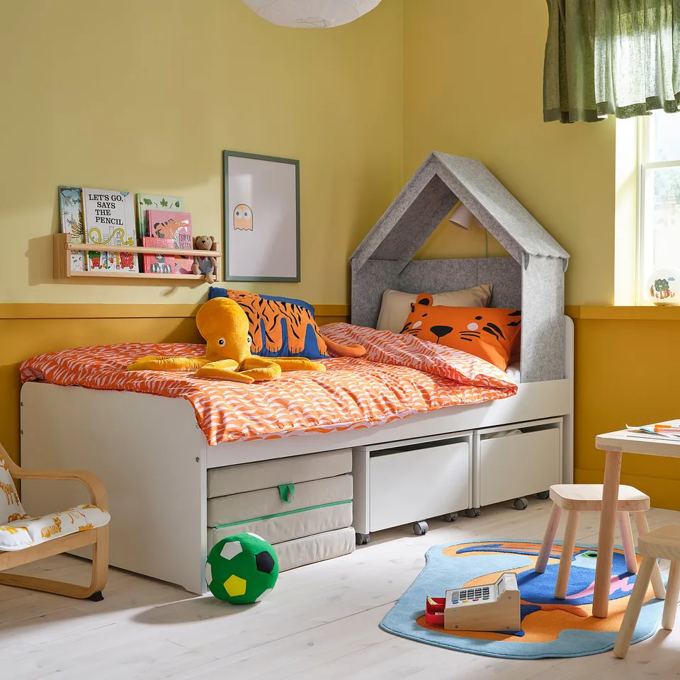 Childs bedroom with house bed, orange bedding, book nook, toys, & green accents.