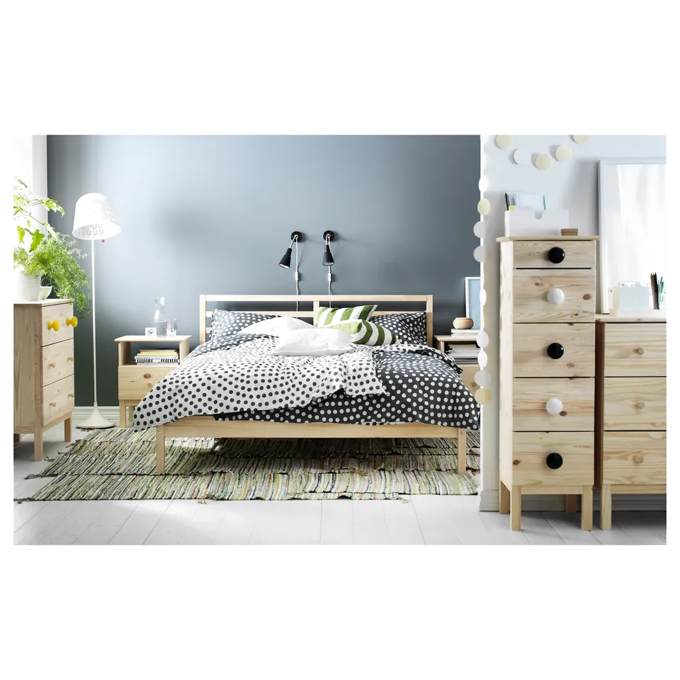 A TARVA bed in natural wood with a polka dot duvet, which scandinavian design elements, positioned between two wooden dressers.