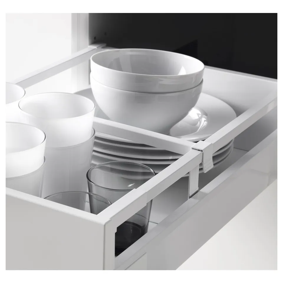 Open kitchen drawer revealing cups, bowls, and plates in white. Soft-close mechanism visible.