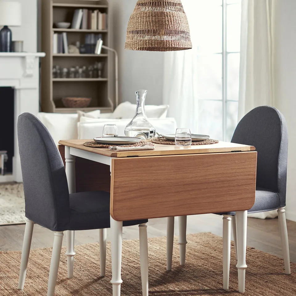 DANDERYD drop-leaf table, natural wood and white, compact with extendable leaves, sat between two grey chairs by a large window.