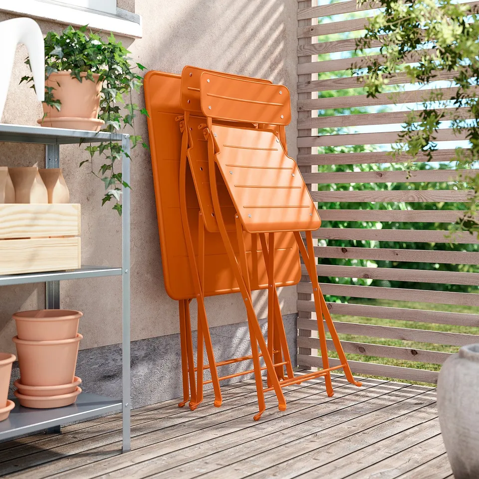 Three bright orange chairs stacked on patio, modern design, near potted plants.