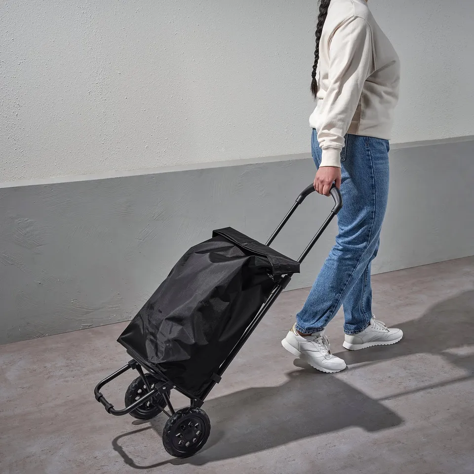 A person pulls a black RADARBULLE bag on wheels; adjustable handle, holds items securely.