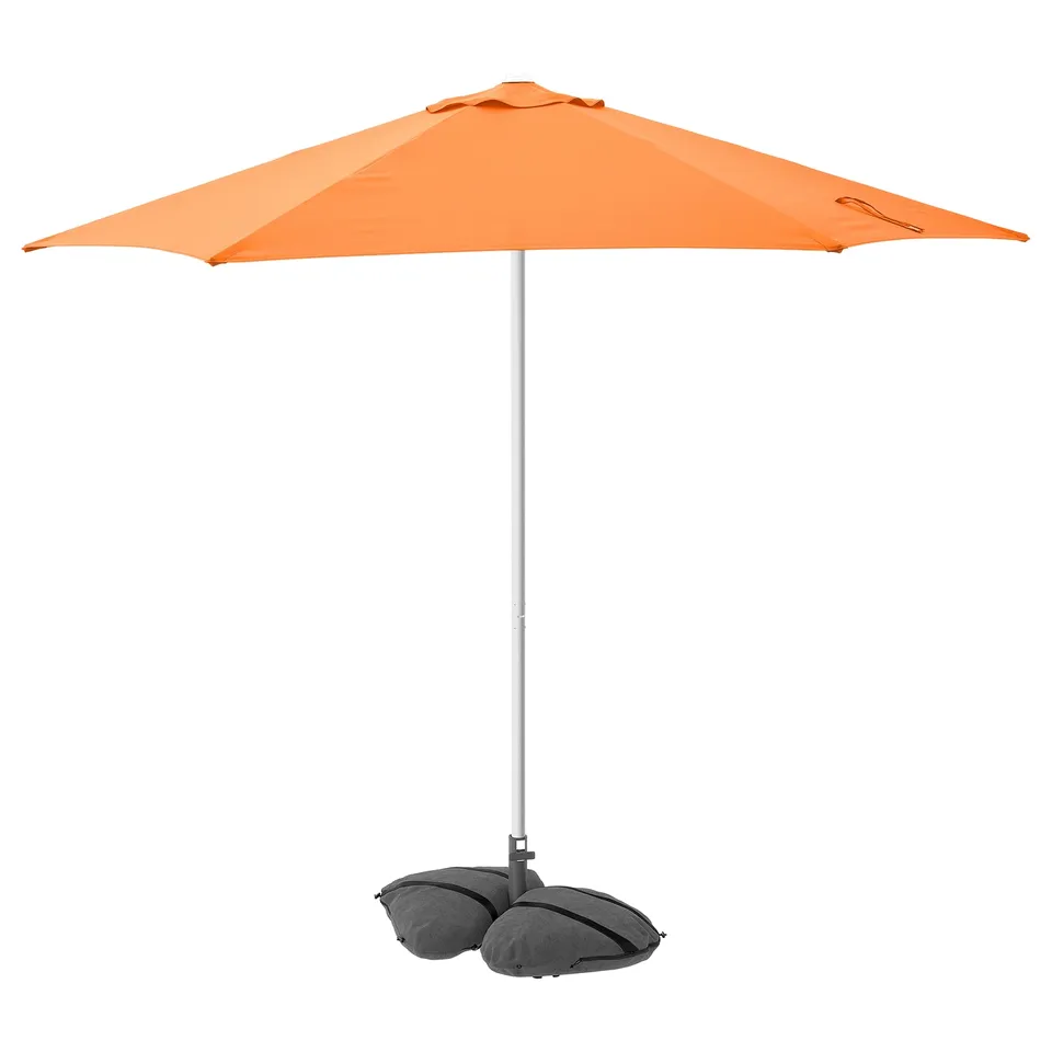 Bright orange HÖGÖN parasol stands tall, supported by grey sandbags, offering uv protection with a robust design.