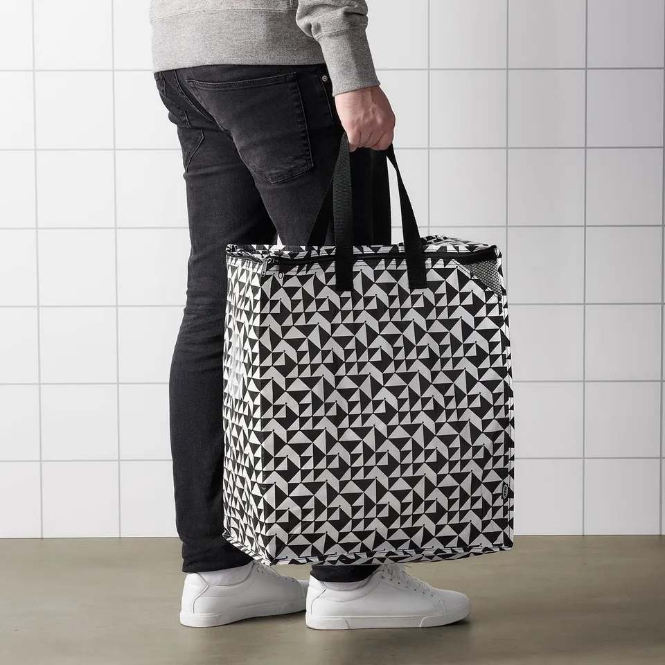 Person holding black and white patterned KNALLA reusable shopping bag.