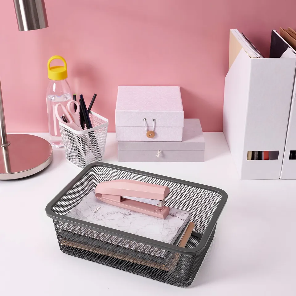 Mesh desk organisers, one with pink stationery, empty one. White box, pastel boxes, supplies container, and yellow-lid water bottle.