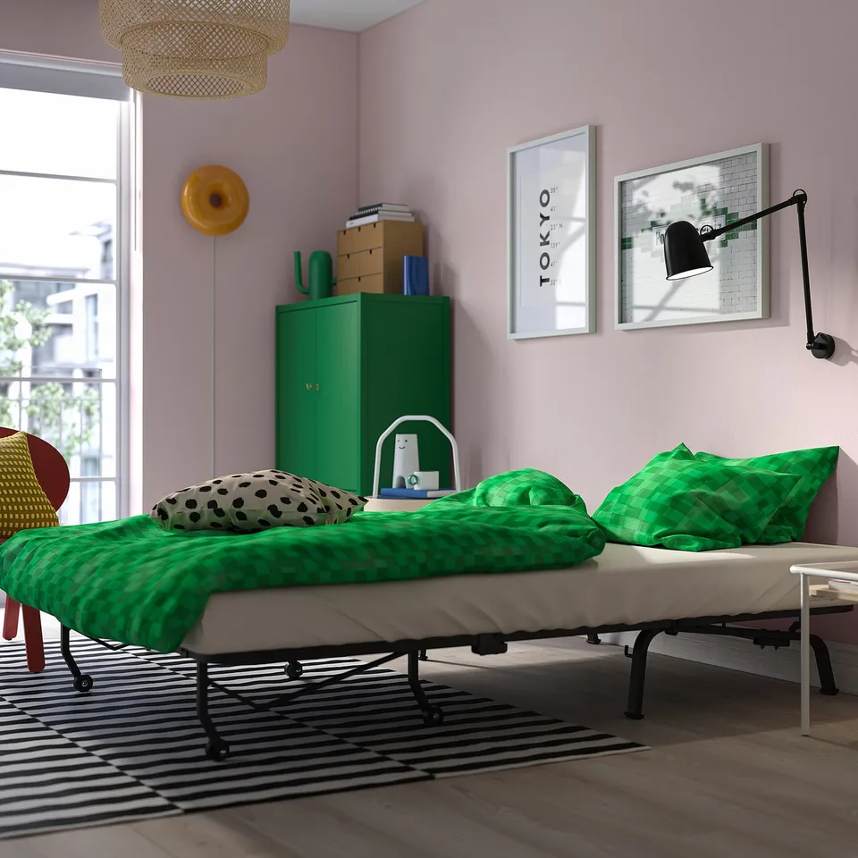 Bright, modern room with green, fold-out bed, green cabinet, striped rug, wall art, and lamp.