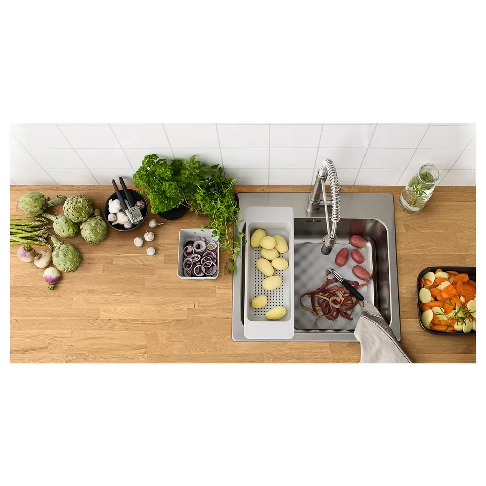 Kitchen counter with stainless steel sink. Wooden surface, vegetables, and fresh herbs.