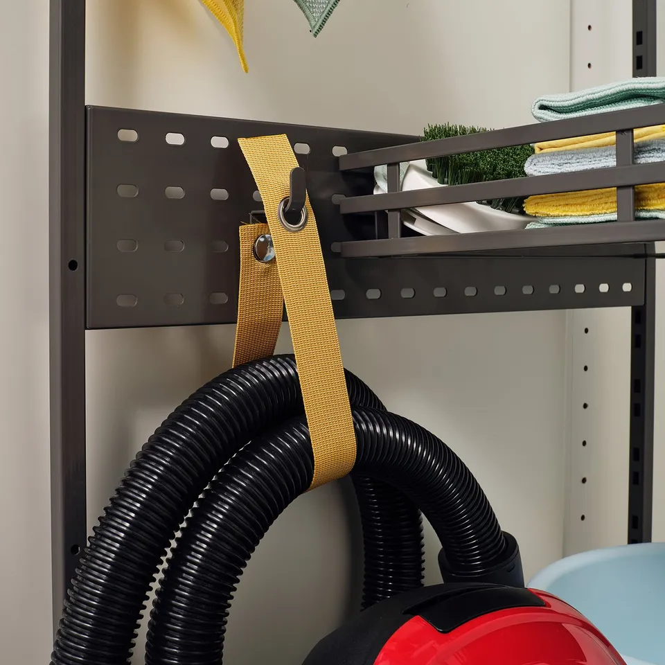 Red vacuum cleaner hangs on yellow strap, organised on black shelf.