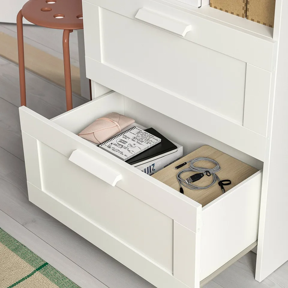 White BRIMNES storage unit with open drawer revealing books and cables. Shown in neat, organised setting.