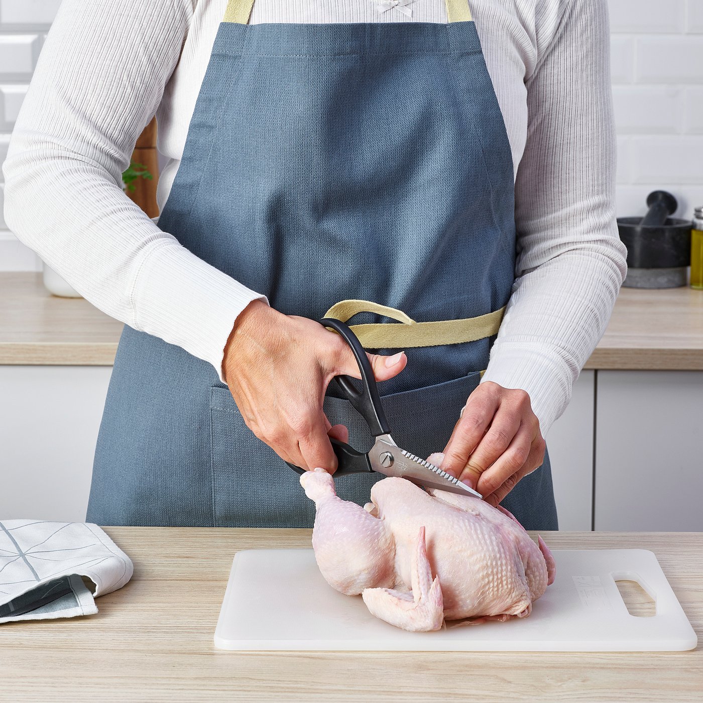Person uses scissors to prepare chicken on cutting board in kitchen.