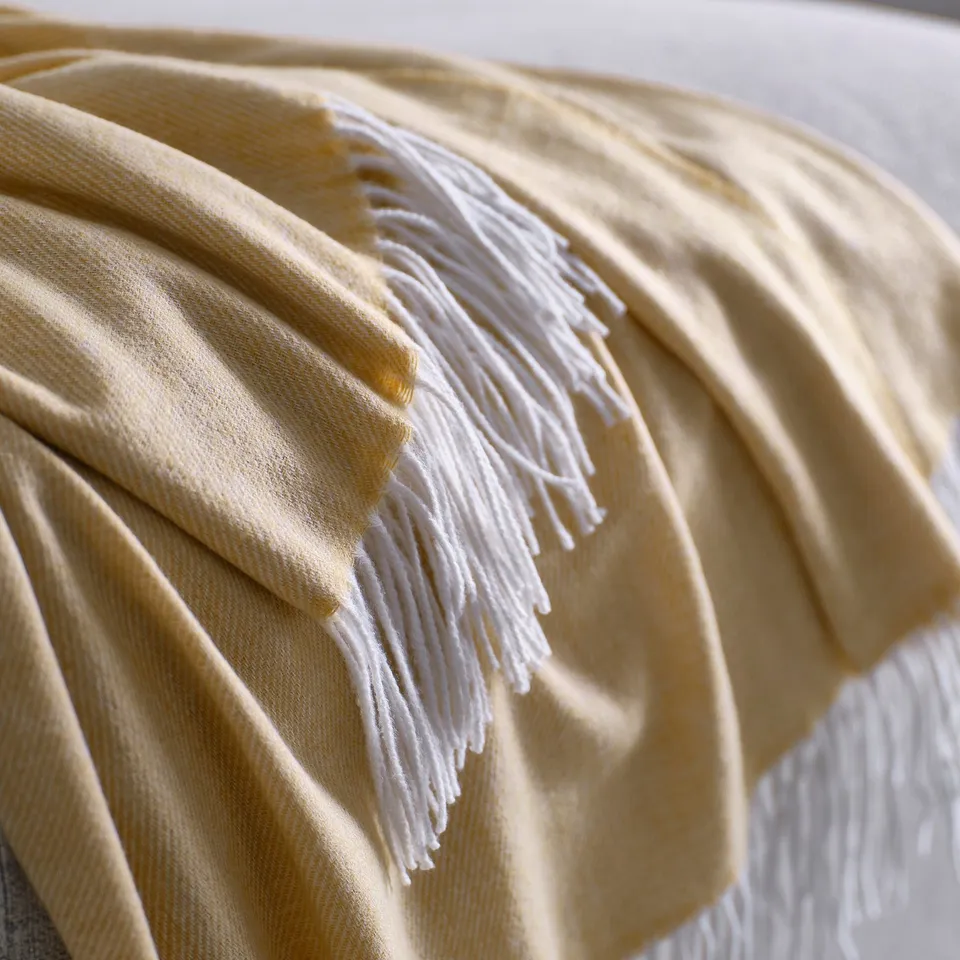 Soft, beige-yellow throw with fringed ends, draped elegantly.