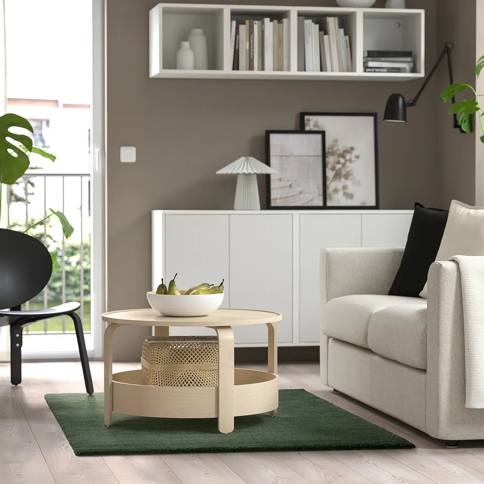 Modern living room with light grey sofa, round light wood coffee table, and large green STOENSE rug.