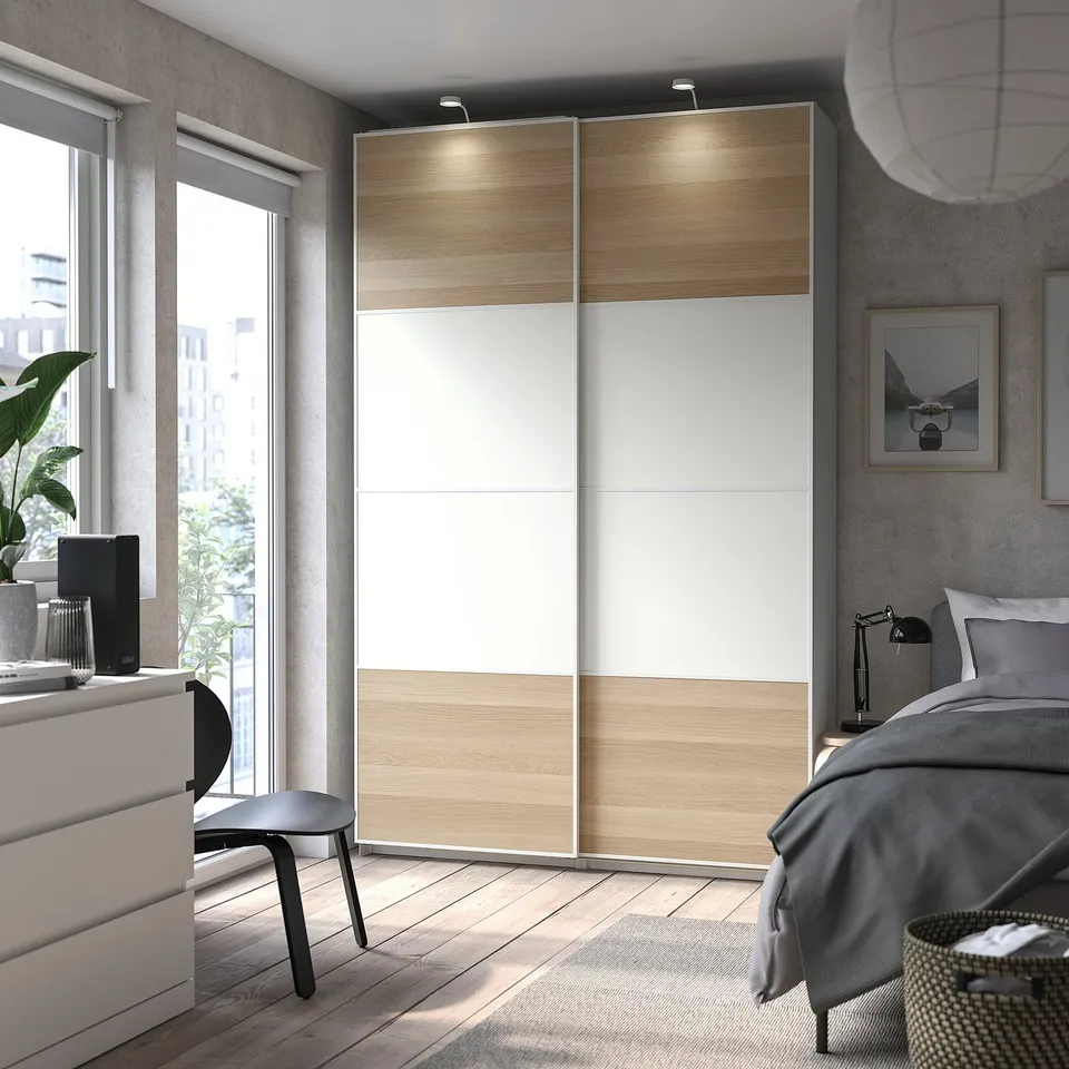 Modern bedroom with light wood and white wardrobe, black furniture, large window, plant, and grey bedding.