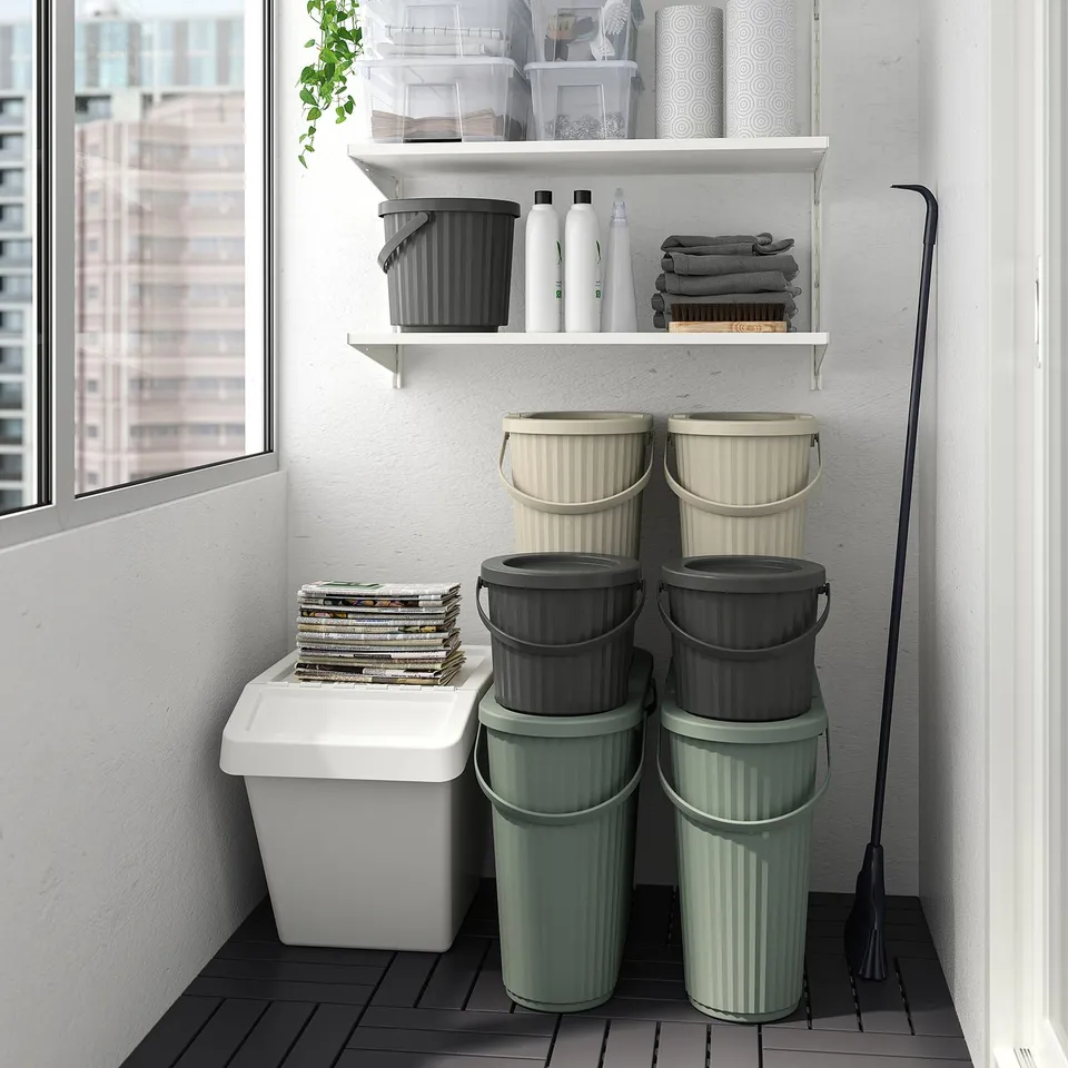 Neatly organised storage with stacked grey and green DAMMÄNG bins for large waste, black broom, and shelved towels and containers.
