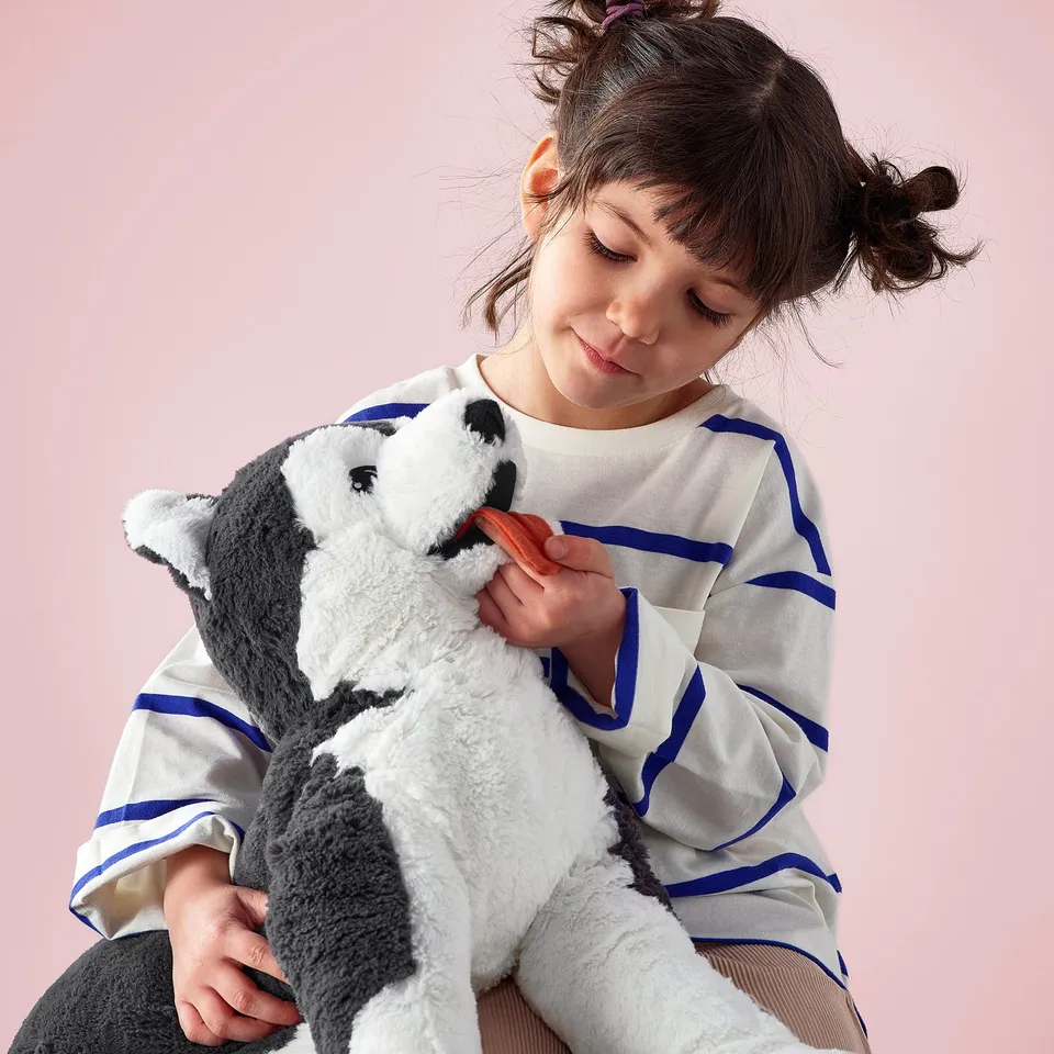 Girl holding gray/white cuddly toy with blue eyes, LIVLIG collection.