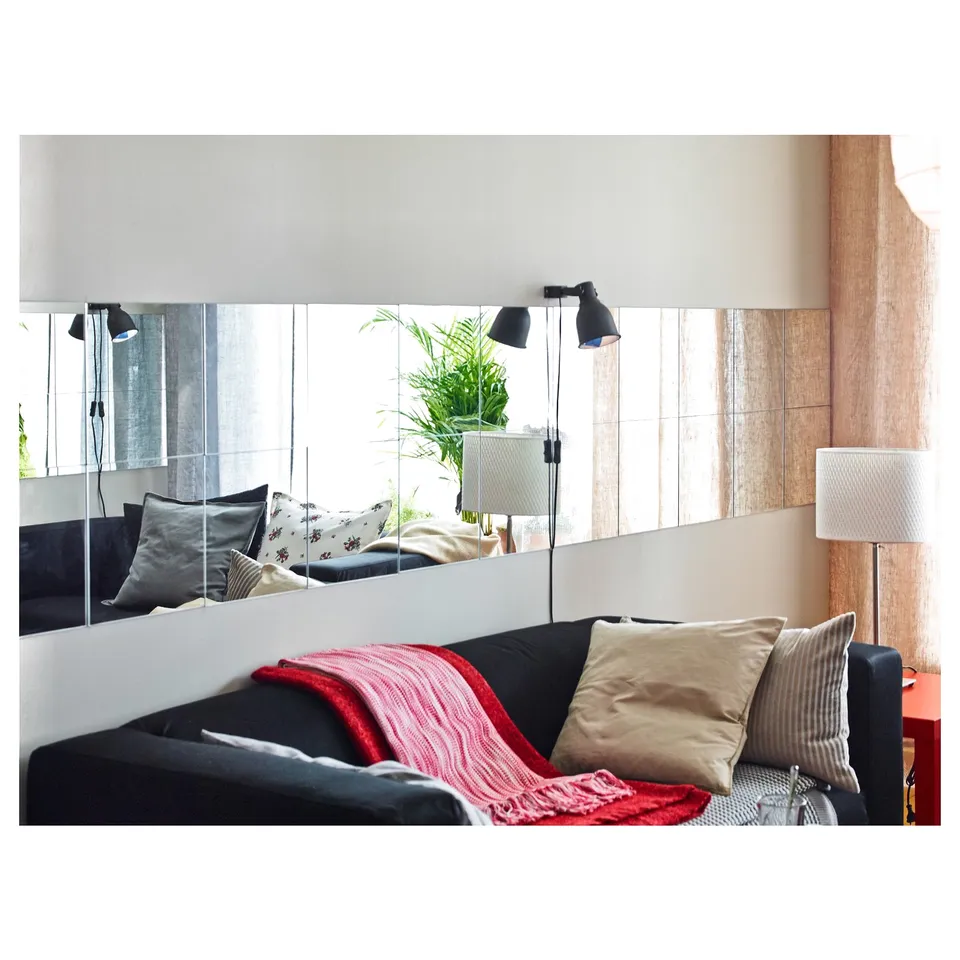 Modern living room with black couch, colourful pillows, mirror wall, and wall lamps.