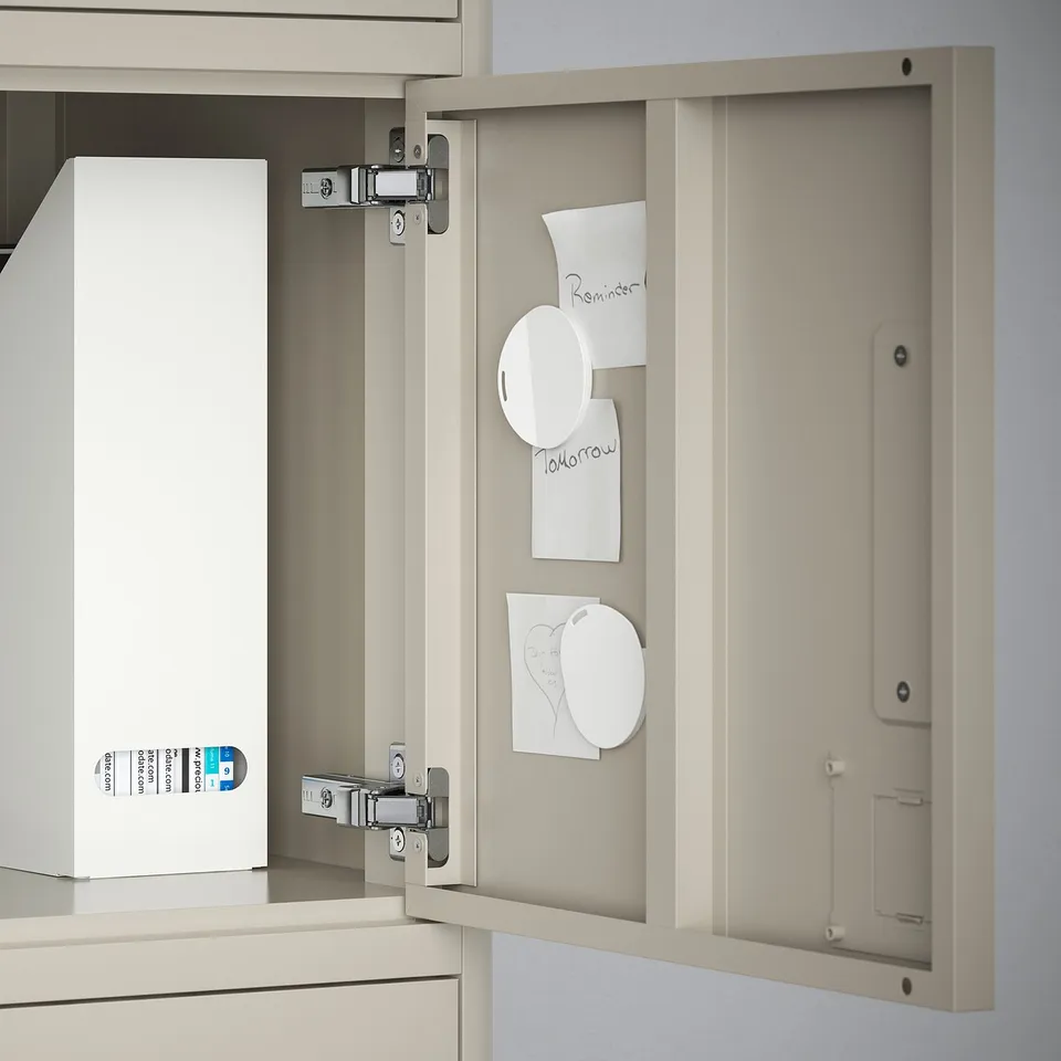 Open beige cabinet door with magnets holding reminders and a white box inside.