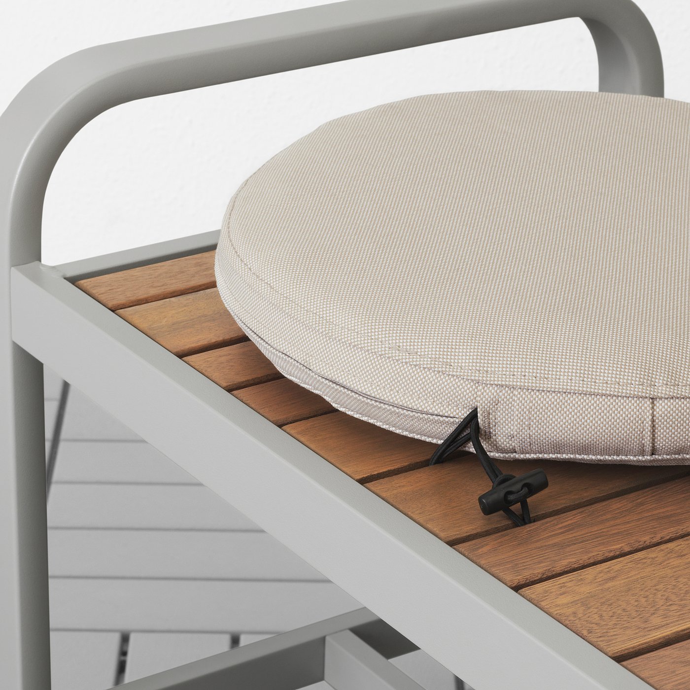 A white cushion with elastic strap attached to a wooden chair. The cushion has a round white cover.