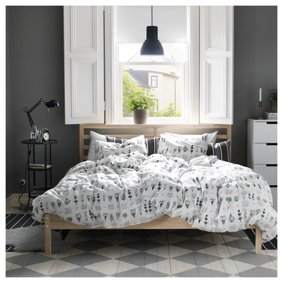 Modern bedroom with TARVA white bed, floral bedding, black lamp, grey cabinets, patterned floor, black pendant lamp.