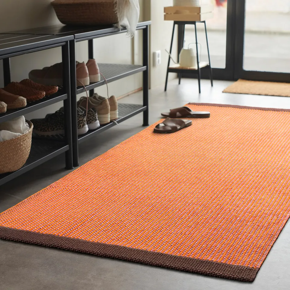 Orange VÄGOMRÅDE rug with slippers and part of shoe rack.