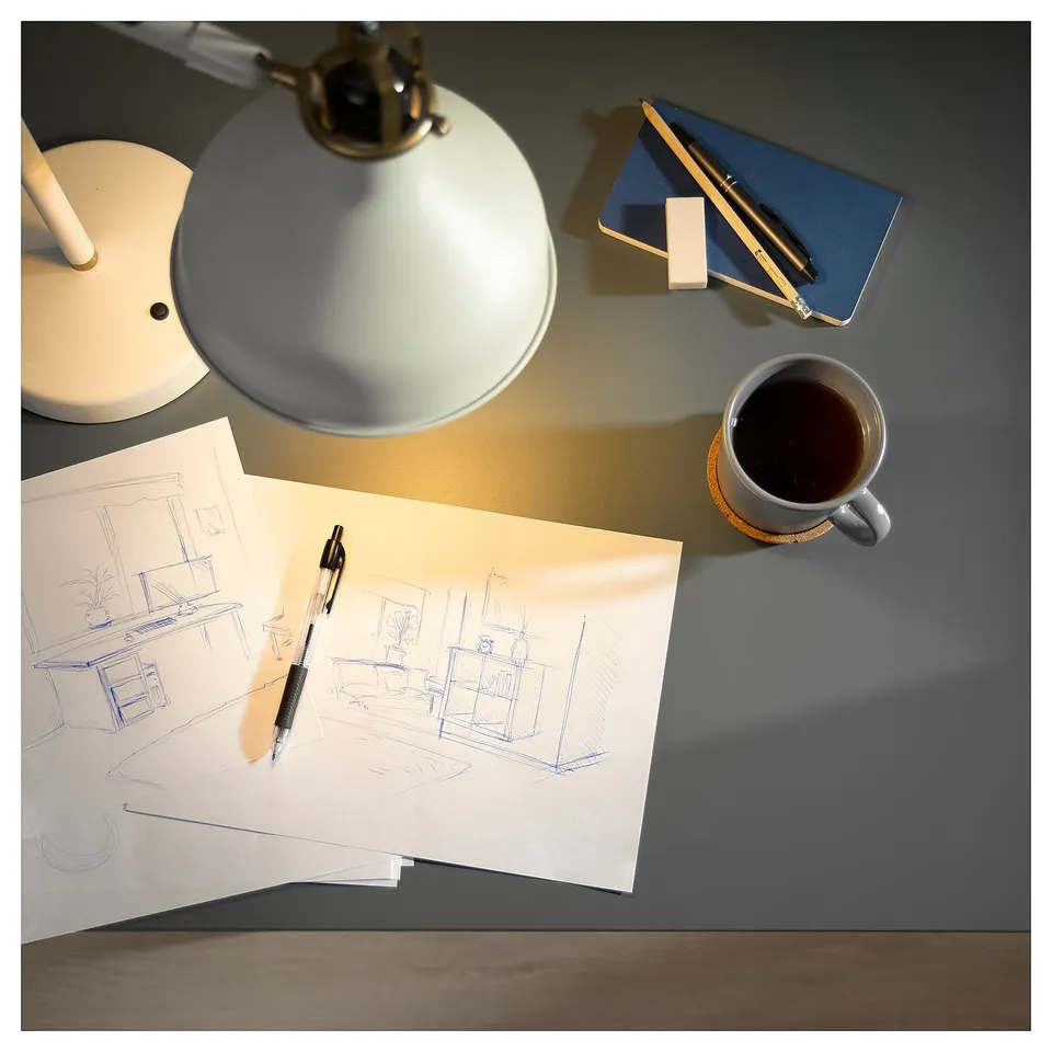 Desk setup with blue notebook, pencil, coffee cup, lamp, and architectural drawings.