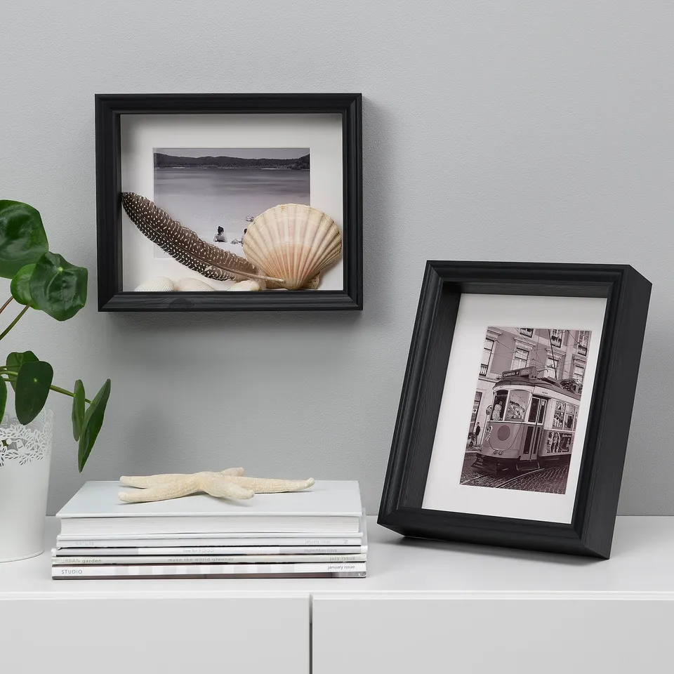 Two picture frames with seashell and city art on shelf, books, plant, starfish.