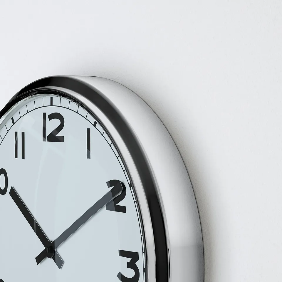 Close-up of clean white clock with black numbers, hands, and stainless rim.