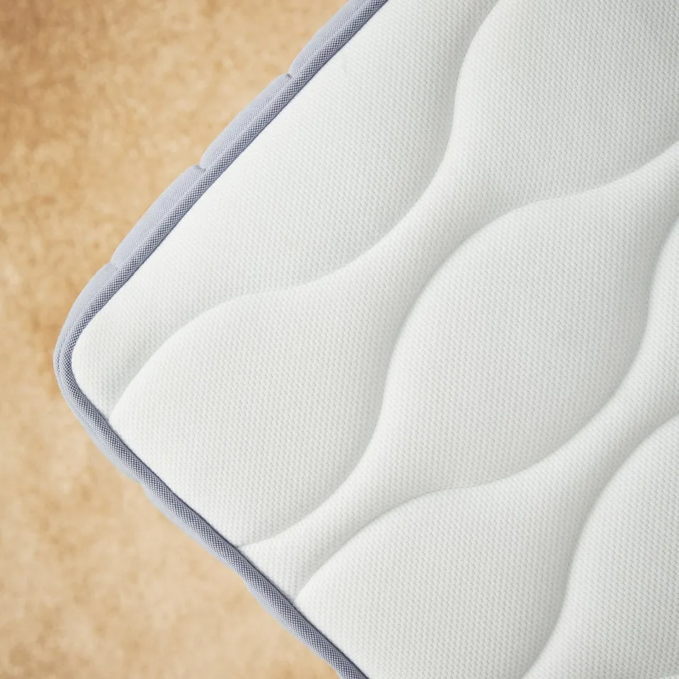 A corner of a VÅGSTRANDA mattress in white with grey edges, featuring a textured surface with wave patterns.