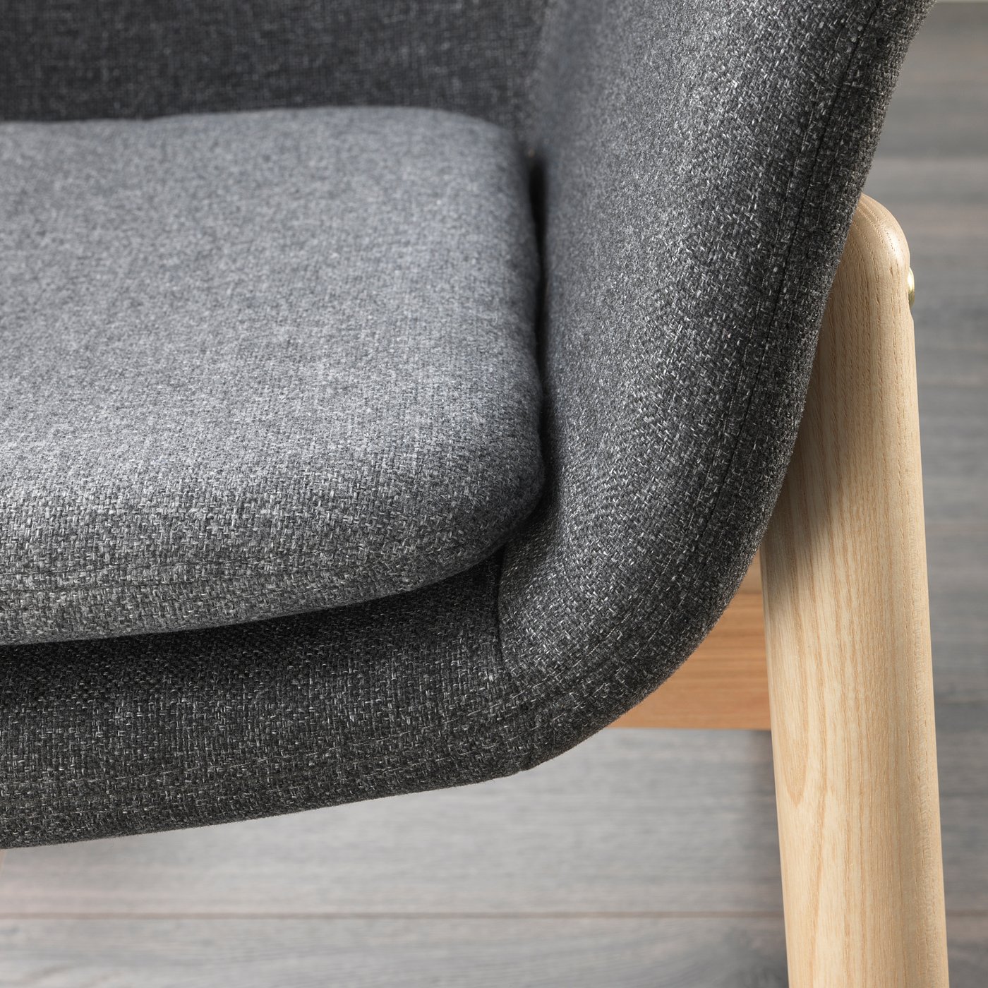 Modern armchair detail: plush grey fabric, sturdy light wood leg.