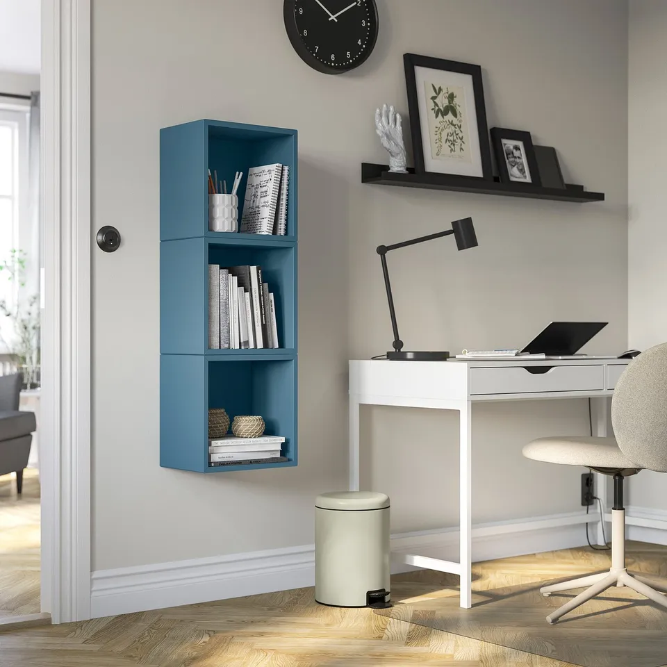Modern home office with blue EKET wall shelves, white desk, and grey chair.
