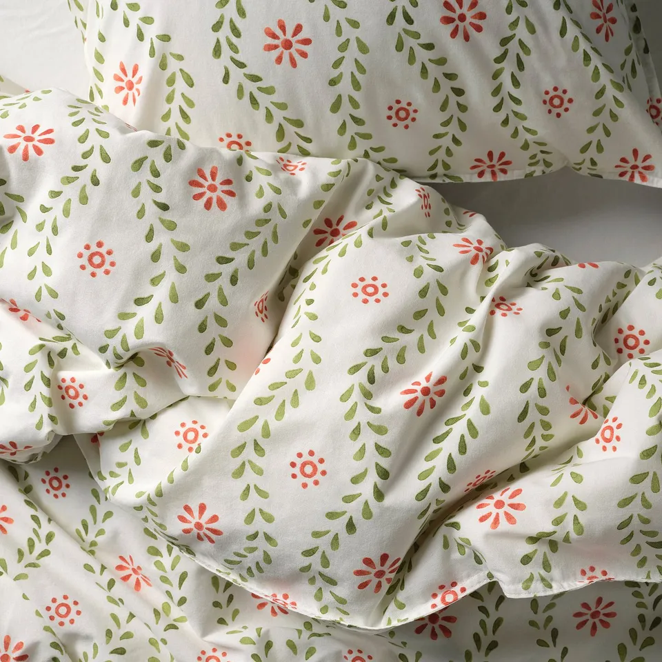 Floral print duvet set with green leaves and red flowers on white cotton, neatly arranged on a bed, showcasing its soft, breathable quality.