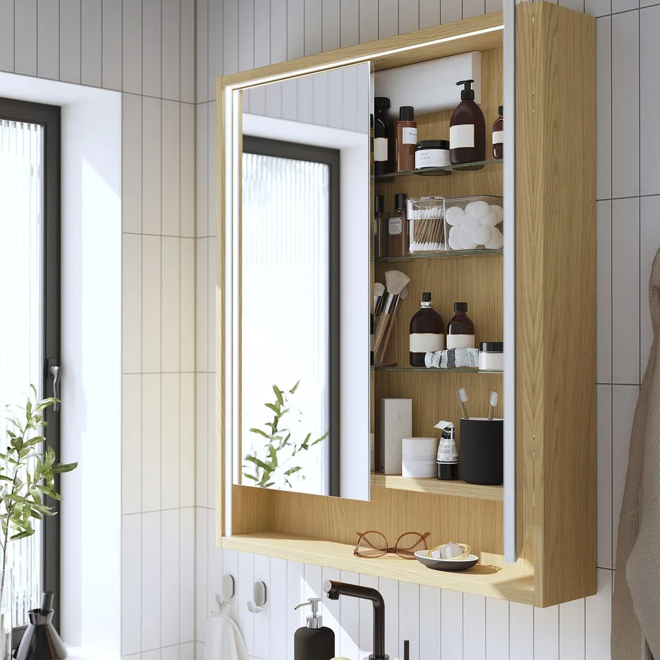 Wall-mounted wooden mirror cabinet with integrated lighting and storage, reflecting a bathroom sink and countertop.