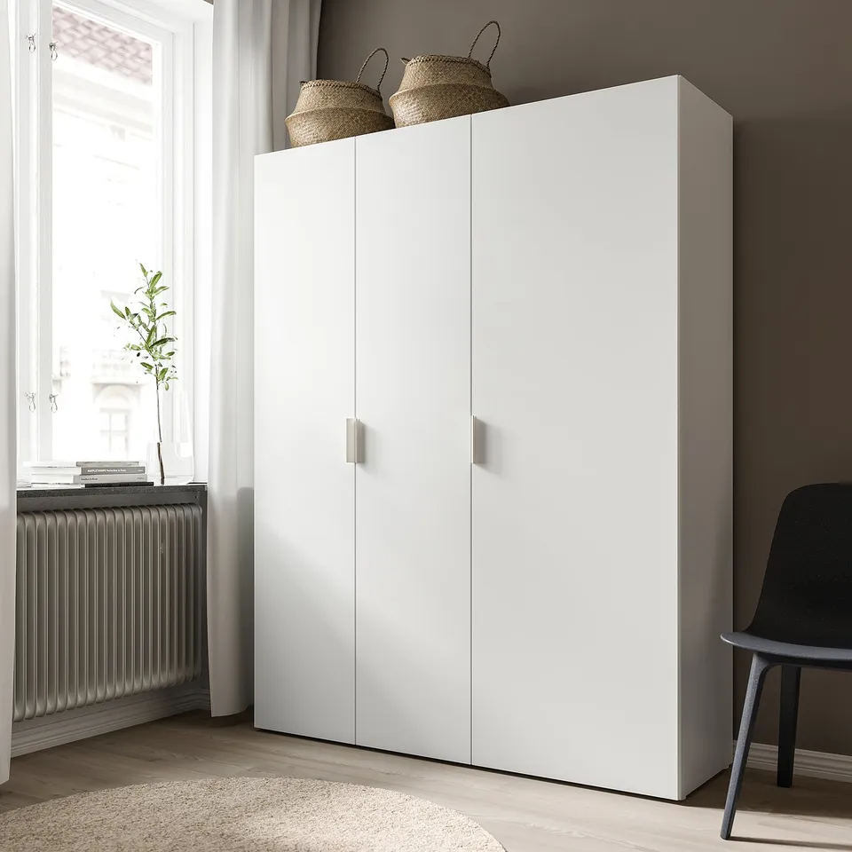 White platsa wardrobe with hinged doors, two wicker baskets on top, near window with plant.