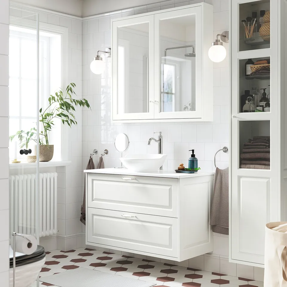White TÄNNFORSEN vanity in modern bathroom. Round basin, bevelled cabinet with drawers, mirrored cabinets, tall storage, white walls, patterned floor.