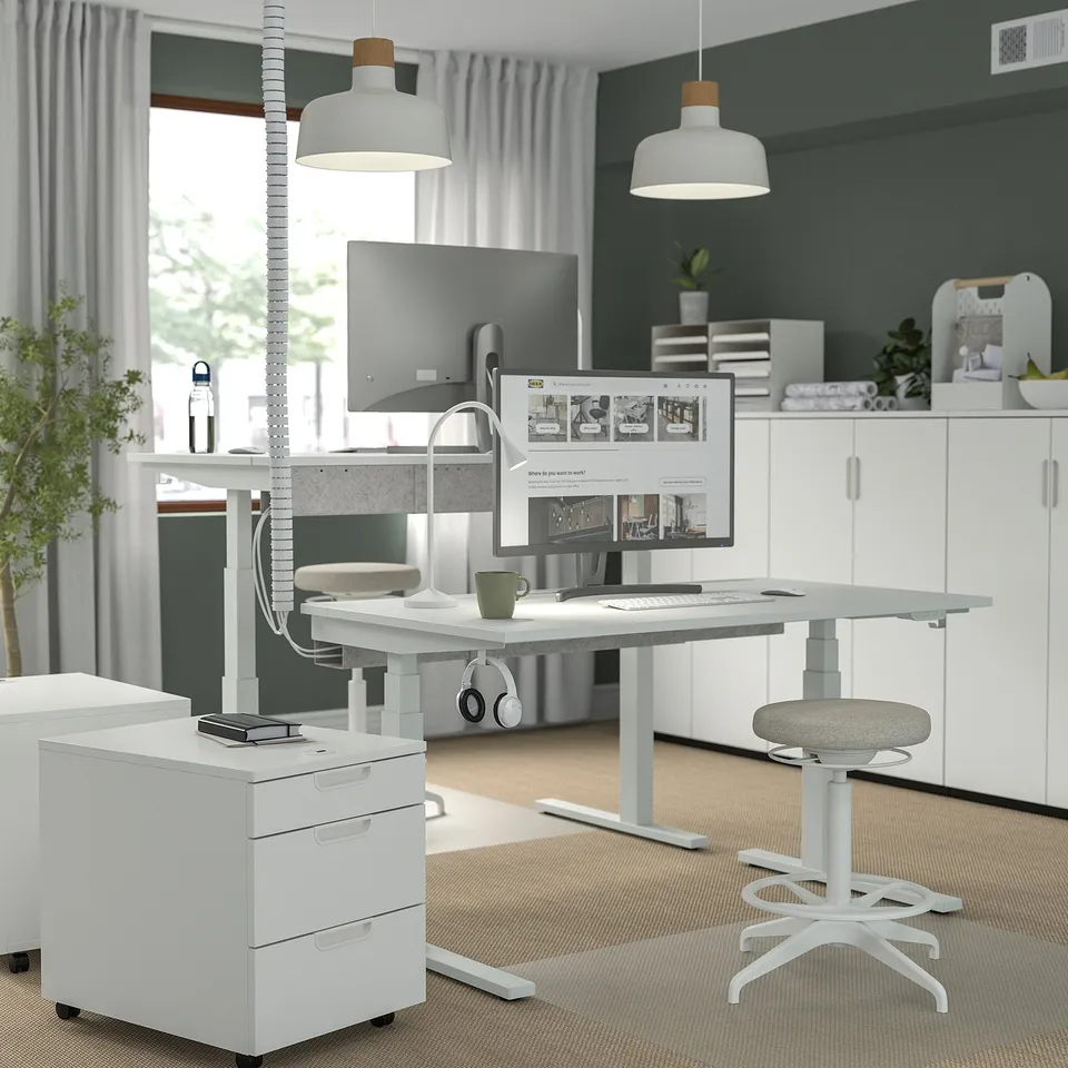 Modern home office with standing desk, dual monitors, ergonomic stool & storage.