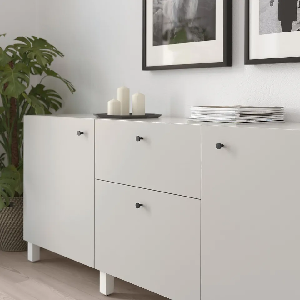 White cabinet with black knobs, decorated with candles and magazines. On wooden floor beside a plant.