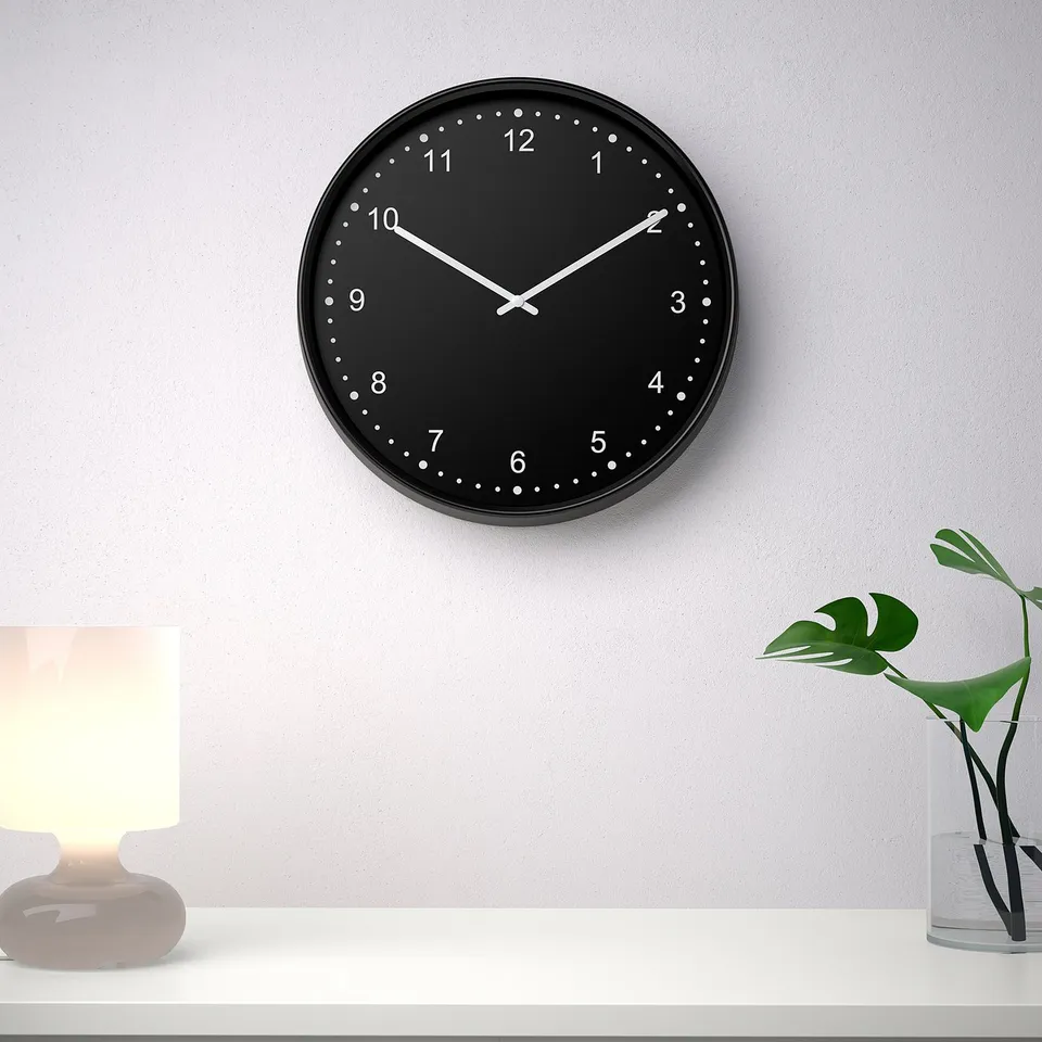 Black wall clock with white numbers in minimalist room. Silent quartz movement, no ticking sounds. Accurate time-keeping.