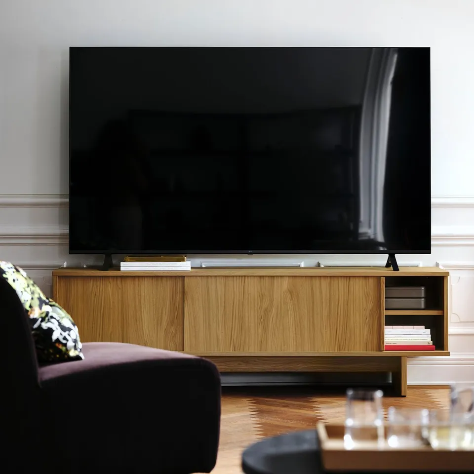 Large flat-screen tv on wooden stand, dark couch left, wine glasses right.