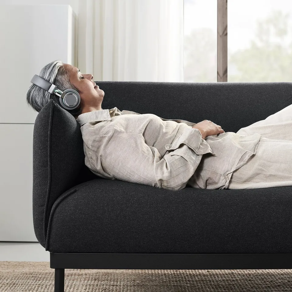 Person relaxing on dark grey ÄPPLARYD sofa, wearing headphones, draped in beige blanket.