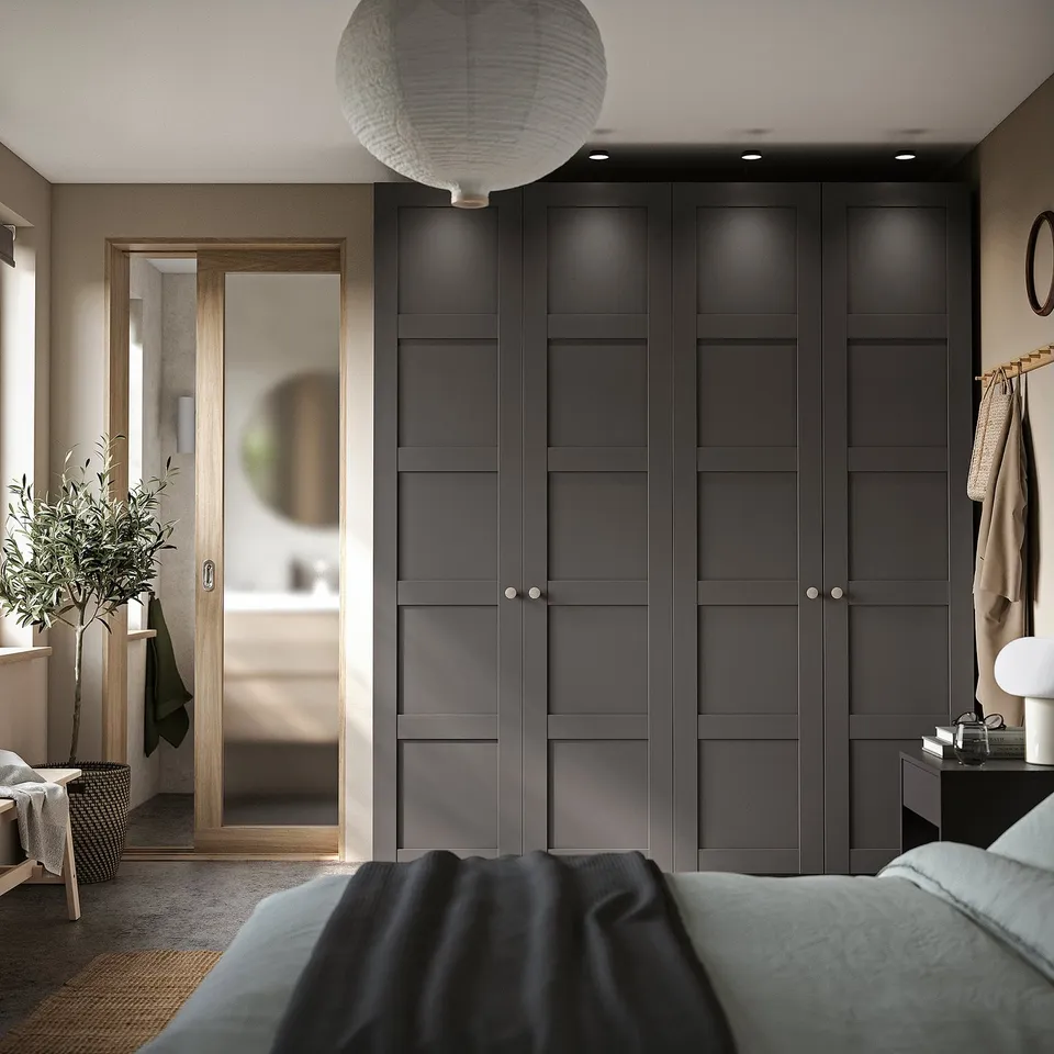 Modern bedroom dark grey PAX wardrobe, tall with six doors, beside glass-walled bathroom. Topped with a white pendant light.