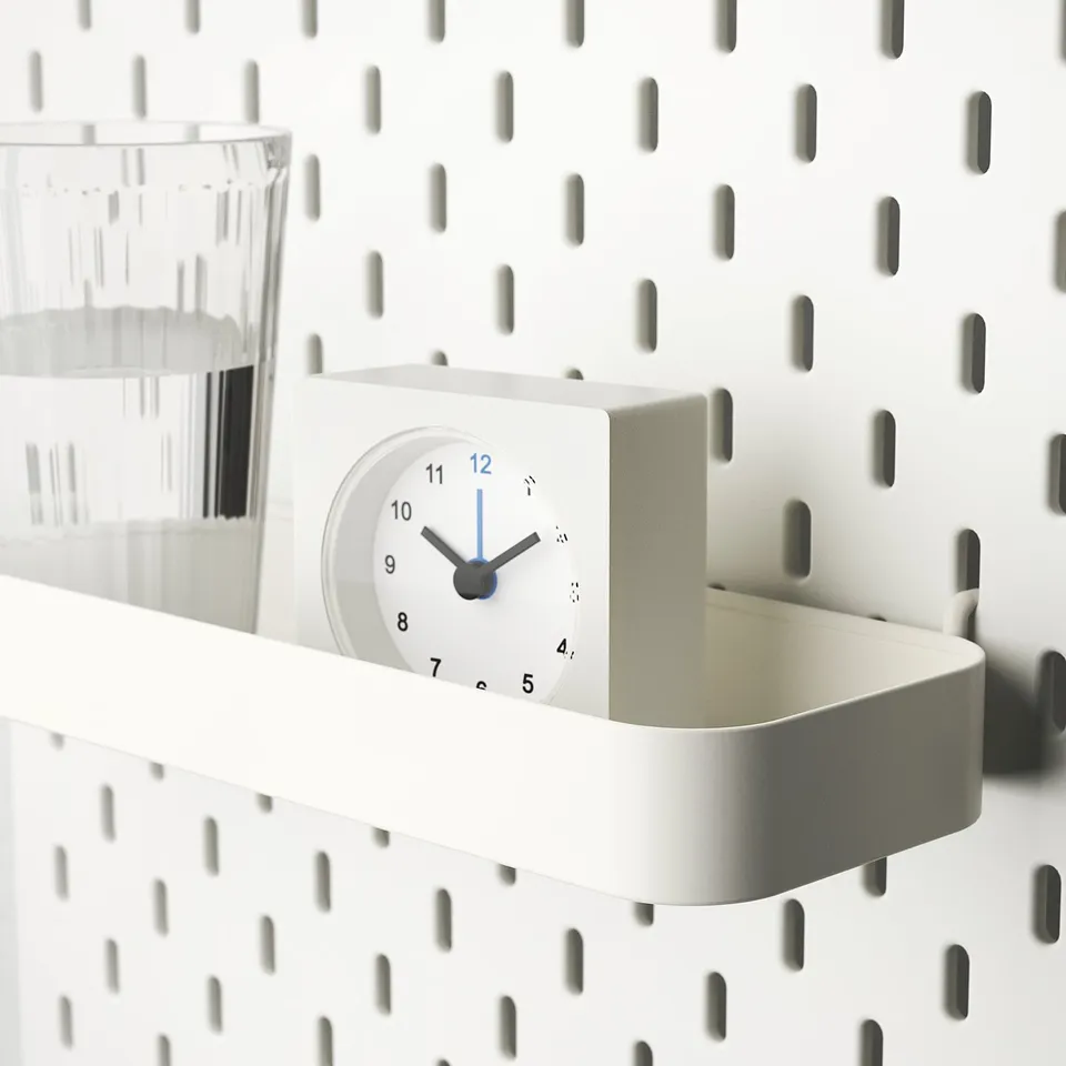 White shelf with clock and container attached to pegboard. Holds small items.